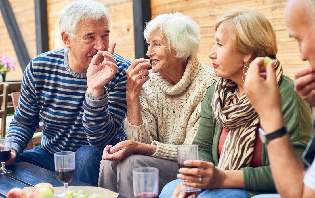 Gruppe gealterter Freunde, die gemeinsam Wein trinken, Snacks essen und reden