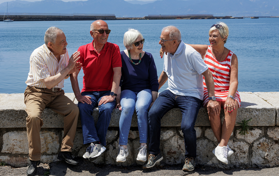 Gruppe älterer Freunde sitzt auf der Mauer an einem See
