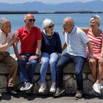Gruppe älterer Freunde sitzt auf der Mauer an einem See - © alex.pin - stock.adobe.com