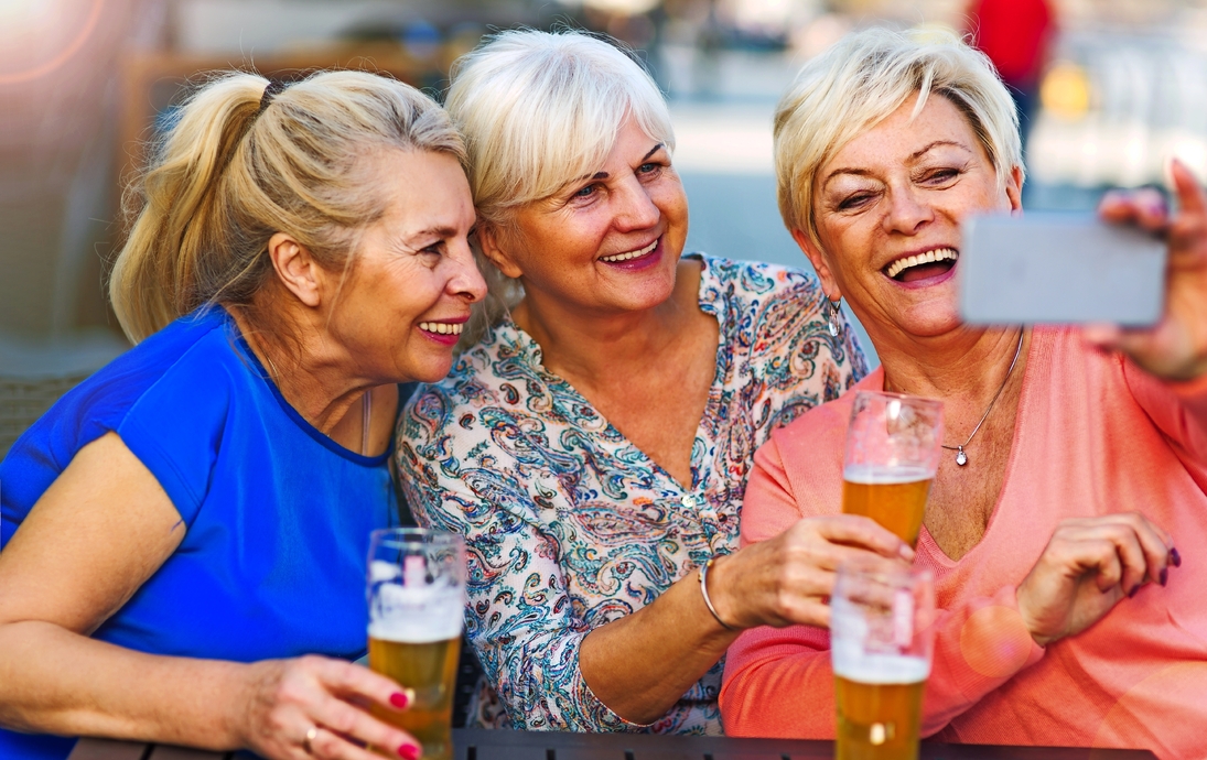 Lächelnde ältere Frauen, die ein Bier in einer Kneipe im Freien essen