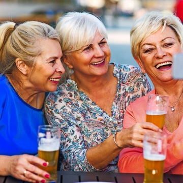 Lächelnde ältere Frauen, die ein Bier in einer Kneipe im Freien essen - © pikselstock - stock.adobe.com